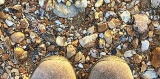 Person,wearing,walking,boots,standing,on,a,pebble,beach,with