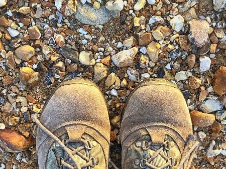 Person,wearing,walking,boots,standing,on,a,pebble,beach,with