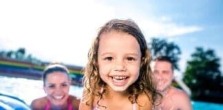 Mother, Father And Daughter In Swimming Pool. Sunny Summer.