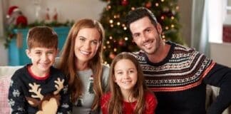 Portrait Of Parents With Children Wearing Festive Jumpers Sitting On Sofa In Lounge At Home On Christmas Day