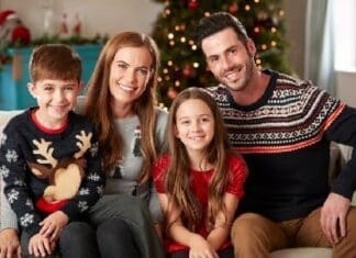 Portrait Of Parents With Children Wearing Festive Jumpers Sitting On Sofa In Lounge At Home On Christmas Day