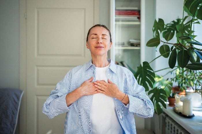 Relaxed Smiling Woman Meditates With Hands On Chest, Practice Breathing Exercises At Home. Self Care