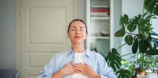 Relaxed Smiling Woman Meditates With Hands On Chest, Practice Breathing Exercises At Home. Self Care