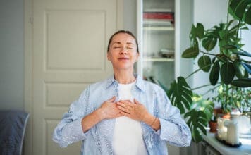 Relaxed Smiling Woman Meditates With Hands On Chest, Practice Breathing Exercises At Home. Self Care