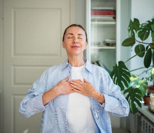Relaxed Smiling Woman Meditates With Hands On Chest, Practice Breathing Exercises At Home. Self Care