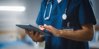 Hospital Ward: Unrecognizable Head Nurse, Doctor, Surgeon Uses Digital Tablet Computer Health Care Vitals Monitoring Computer Machine. Modern Clinic With Advanced Equipment And Professional Working