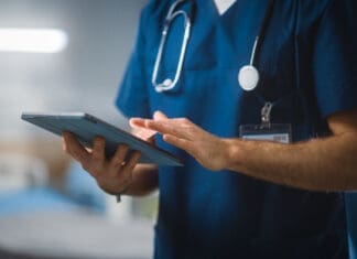 Hospital Ward: Unrecognizable Head Nurse, Doctor, Surgeon Uses Digital Tablet Computer Health Care Vitals Monitoring Computer Machine. Modern Clinic With Advanced Equipment And Professional Working